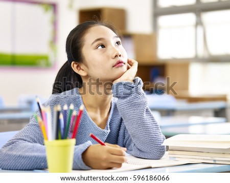 asian elementary schoolgirl looking up and thinking while studying in classroom. Royalty-Free Stock Photo #596186066