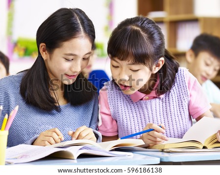 two asian elementary schoolgirls desk mates having a discussion during class in classroom. Royalty-Free Stock Photo #596186138