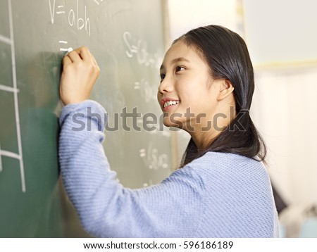 confident asian elementary school student writing the answer to a geometry problem on blackboard. Royalty-Free Stock Photo #596186189