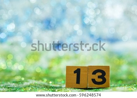 Number "Thirteen" made by wooden block on blurred glitter background.