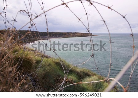Allied Invasion D-Day World War II memorial landing site at Normandy Utah Beach France along English Channel view of curved coastal bluff coastline with barbed wire in foreground under dramatic sky
