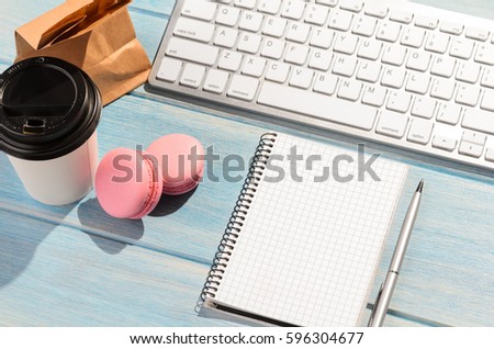 Working on the go. White modern keyboard with coffee cup, candies and notepad on blue wooden table at sunny weather
