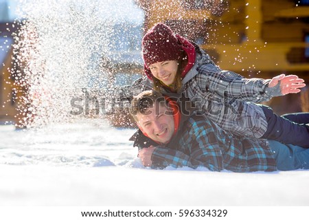 Young couple lies on the snow. The girl climbed onto the back of her boyfriend and sprinkled it with snow. Between them comic fight. Sunny winter day. Good mood. Young people smile