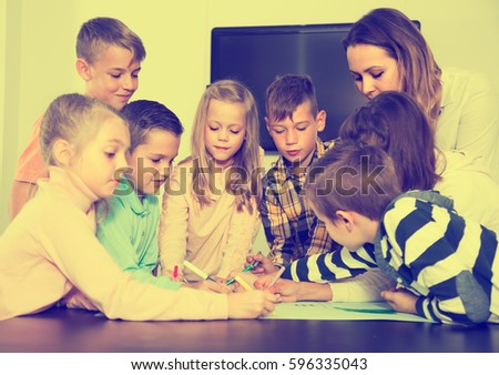 Professor and elementary age children drawing together one picture in classroom