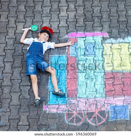 Happy little kid boy having fun with train or steam locomotive picture drawing with colorful chalks on ground. Children, lifestyle, fun concept. funny child playing and dreaming of future profession.
