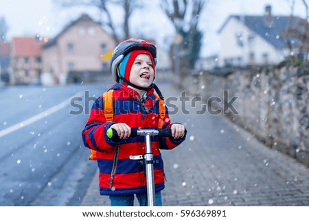 Cute little preschool kid boy riding on scooter riding to school. children activities outdoor in winter, spring or autumn. funny happy child in colorful fashion clothes and with helmet. High speed