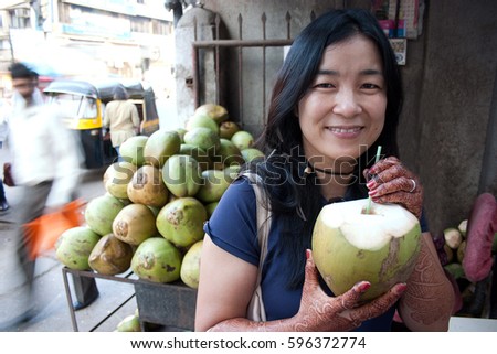 Adult Japanese woman with henna tattoo drinking coconut water in India Royalty-Free Stock Photo #596372774