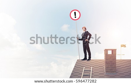 Young businessman with roadsign in hand standing on brick roof. Mixed media