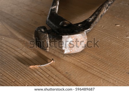 Closeup of rusty crooked nail and old pliers on dusty wooden board.
