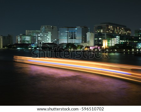 Building near the river and a orange with blue light line of boat on the river, hospital riverside, at night