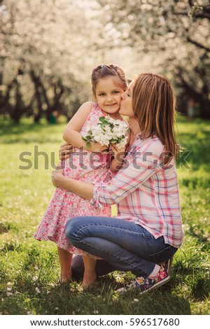spring vertical portrait of happy mother and kid daughter on the walk in blooming cherry garden. 