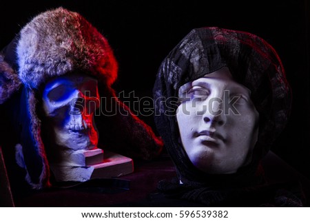 A colorful still life of an artificial skull and a female face statue. Blue and red studio lights and artistic composition