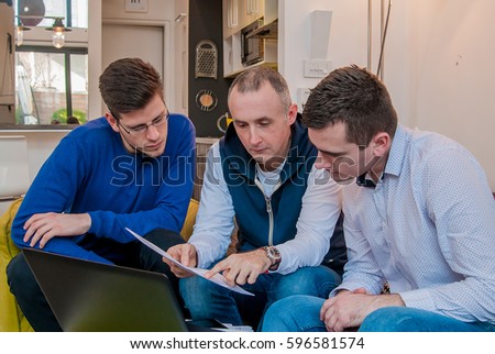 Photo of a group of friends working on some new ideas at home. Young business people are studying documents, discussing ideas and smiling while working at home