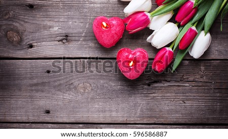 Two red  burning candles in form of  heart  and bright  spring  tulips flowers on rustic wooden background.  Selective focus. Flat lay. Place for text. Toned image.