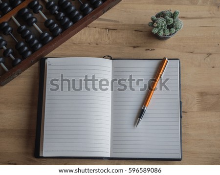 top view of open book with pen,abacus and cactus in pot on wooden desk