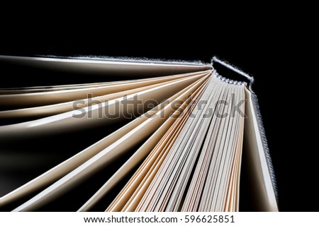 Open blank notebook in sun light. Warm atmosphere and black background. Pages stand vertically open as fan of flying paper. Abstract texture of thick white and yellow paper for writing or drawing