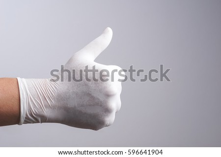 Hand wearing latex glove with thumb up gesture on white background