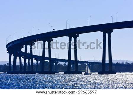 Small sailboat under the San Diego - Coronado Bridge, locally referred to as the Coronado Bridge, crossing over San Diego Bay in the United States, linking San Diego, with Coronado, California.