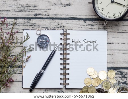 Travel conceptual image with HELLO SUMMER word on notebook with pen, compass, alarm clock, coins in jar and wooden background