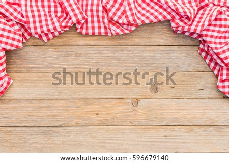 Red checked tablecloth frame on wooden table background.