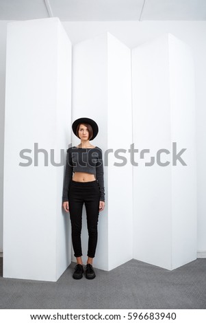 Young beautiful girl in black hat posing over white background.