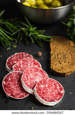 Salami sausage sliced with rosemary, olives and spices on the dark background. Shallow depth of field.
