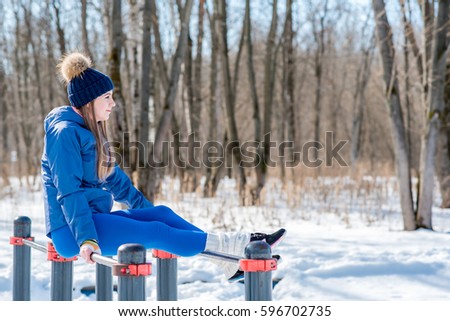 Beautiful young girl doing stretching, fitness on a sports field in winter against a background of deciduous forest.  sports concept photo