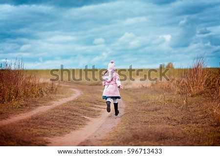 Little girl in pink coat walking down the path in the field in autumn outdoor
