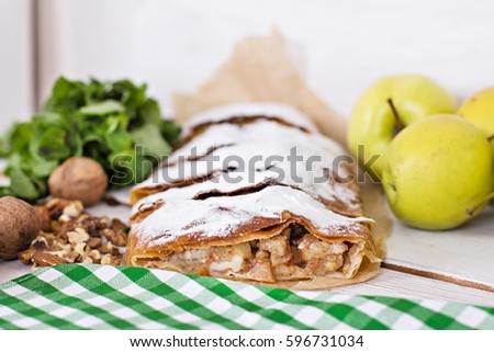 Sliced homemade apple strudel served with fresh apples, cinnamon sticks, mint and sugar powder over white wooden background. Close up, dark rustic style Apple strudel.