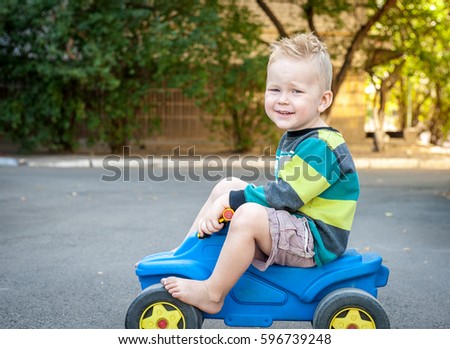 Cute little happy boy in toy car. background summer park. Funny boy car driver. Baby kid toddler playing, driving outdoors. Educational toys for preschool and kindergarten child.  Car trip playground