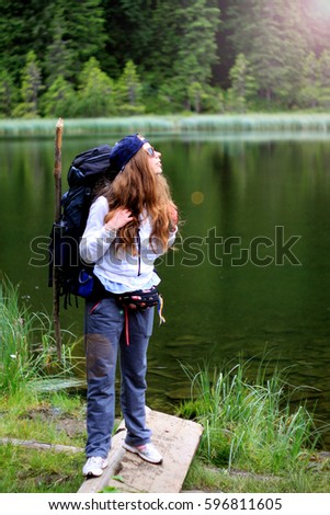 Beautiful blonde female traveler with backpack smiling. Mountain lake background. Travel and freedom concept.