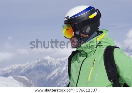 Portrait of an adult male in a ski helmet and glasses, with high snow mountains in the background