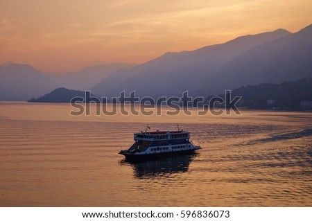 Colorful sunset at Lake Como, Italy on a nice early autumn day with hills & mountains surrounding the Italian lake & a ferry boat sailing on the water. This picture was taken from Bellagio looking SW.