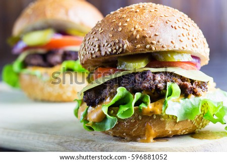 Tasty burger cheeseburger with tomato, lettuce and veal cutlets on rustic brown wooden table, close-up, selective focus