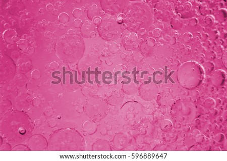 Lightly illuminated slightly blurred perfect round spheres of immiscible liquid of varying sizes background reddish pink color