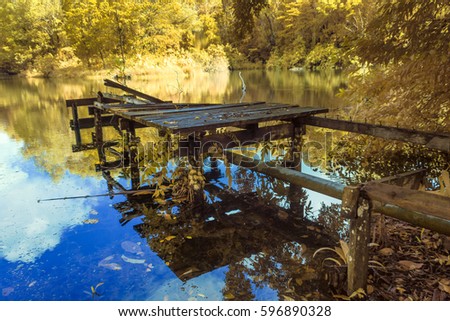 Abandoned wooden jetty in calm lake with reflection of tropical trees in Labuan,Malaysia.View in infrared photography,soft focusing.