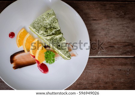 Green tea cake with orange topping in white plate on wooden table.