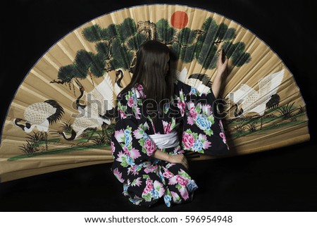 Japanese girl in traditional Japanese kimono with a large fan on a black background. Isolated photo.