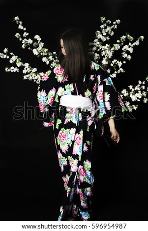 Japanese girl in traditional Japanese kimono, holds sprigs of cherry blossoms on a black background. Isolated photo.