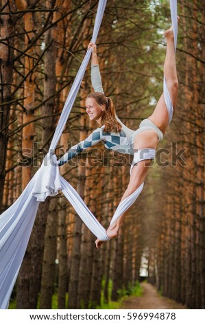 Beautiful, slim gymnast doing the difficult exercises on the silks in the forest