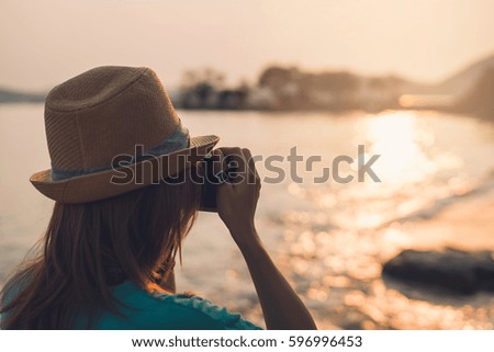 Young woman traveler taking photo on the beach at beautiful sunset