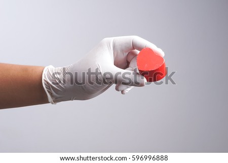 Hand wearing latex glove holding wooden heart shape object on white background