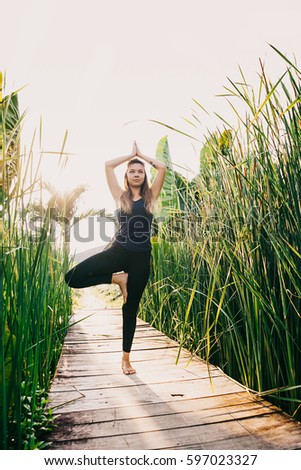 Young woman practicing yoga during luxury yoga retreat in Asia, Bali, meditation, relaxation, getting fit, enlightening, green grass jungle background