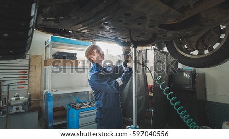 Worker Mechanic unscrewing parts of automobile's bottom under lifted car