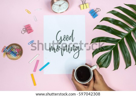 Feminine desk workspace with quote Good morning written in calligraphic style on paper on pink background. Flat lay, top view.