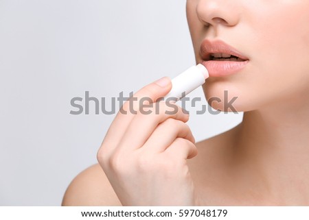 Woman applying hygienic lip balm on light background Royalty-Free Stock Photo #597048179
