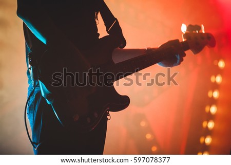 Silhouette of bass guitar player with colorful stage illumination, live rock music theme