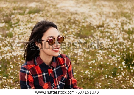 Beautiful woman with sunglasses sitting in the middle of a flowery meadow
