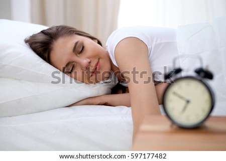 Sleepy young brunette woman stretching hand to ringing alarm willing turn it off. Early wake up, not getting enough sleep concept Royalty-Free Stock Photo #597177482