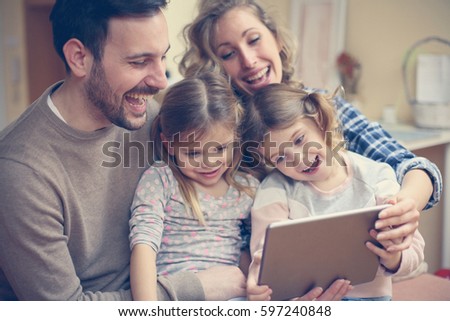 Happy family spending time at home and looking something fanny on tablet. Royalty-Free Stock Photo #597240848